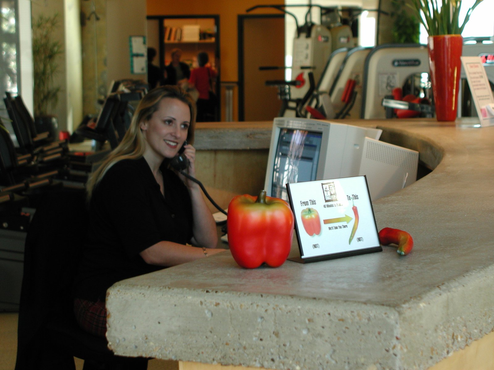 Personal training studio receptionist on the phone at curved front desk with cardio equipment in the background