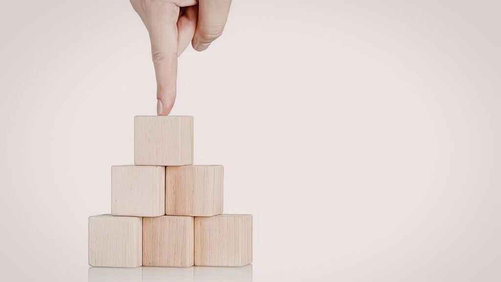 Hand stacking wooden blocks, representing the 6-week foundation phase built step by step for a personal training business